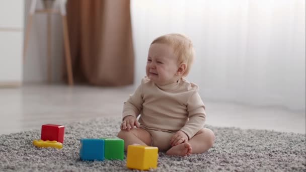 Síró csecsemő fiú ül a padlón a nappaliban játékok körül — Stock videók