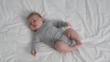 Cute Plump Newborn Baby In Grey Bodysuit Lying On Bed At Home