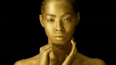 Female With Golden Skin Posing Touching Face Over Black Background