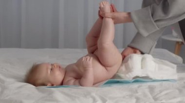 Unrecognizable Mother Changing Diaper To Her Cute Newborn Baby Lying On Bed