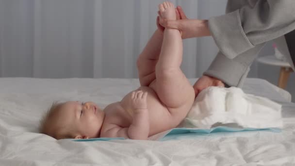 Неузнаваемая мать, меняющая подгузник на свою милую новорожденную малышку, лежащую на кровати — стоковое видео