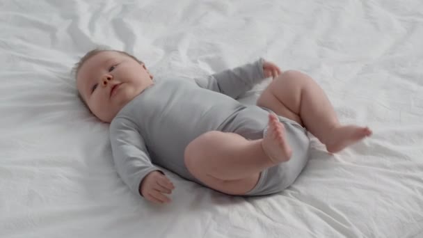 Симпатичный новорожденный, лежащий на кровати дома, двигающий ногами и руками — стоковое видео