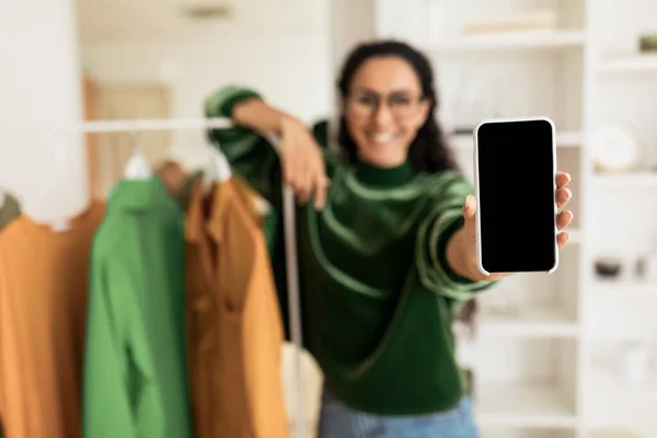 Femme méconnaissable montrant écran Smartphone debout près de rail de vêtements à l'intérieur — Photo