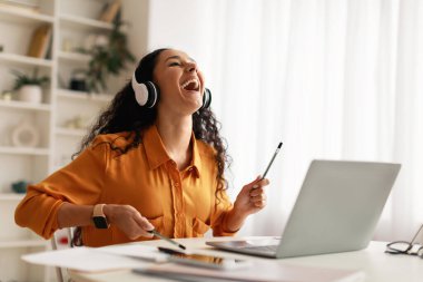 Lady Wearing Earphones Pretending Playing Drums Sitting At Laptop Indoor