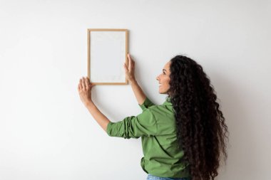 Lady Hanging Picture In Frame On Wall Decorating House Indoors