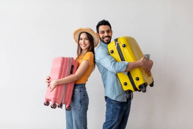 Heyecanlı genç turistler yurtdışına seyahat etmeye hazır, bavullarını ellerinde tutuyorlar ve kameraya gülümsüyorlar, ışık duvarı.