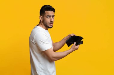 Unhappy arabic man showing empty wallet at studio