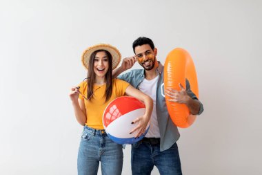 Excited married couple standing with an inflatable circle and ball on light background wall, free space