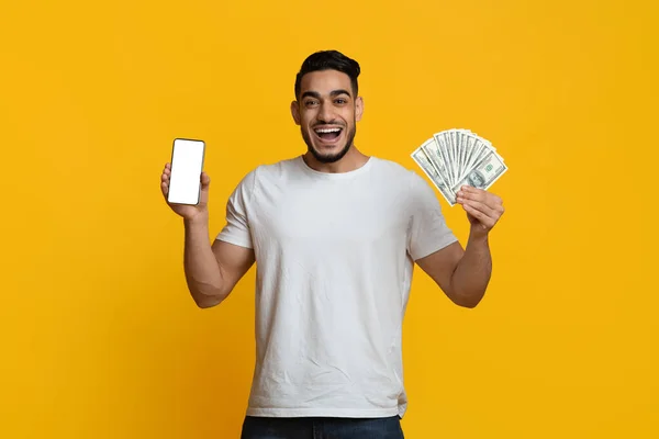 Emocional chico de Oriente Medio mostrando teléfono inteligente y dinero en efectivo —  Fotos de Stock