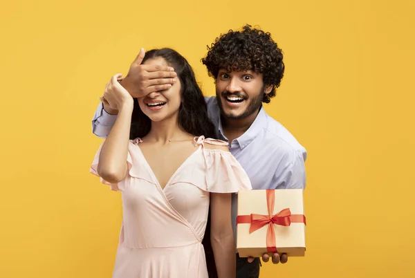 Happy anniversary. Loving indian man covering his girlfriends eyes, greeting her with wrapped gift box — Fotografia de Stock