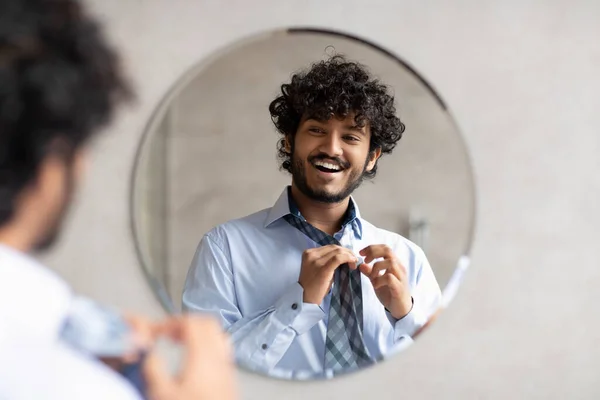 Щасливий індійський бізнесмен одягає краватку, дивлячись у дзеркало, стоячи в сучасній ванній кімнаті, вільний простір — стокове фото