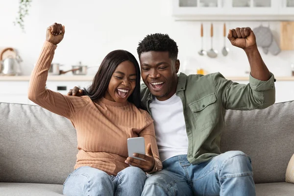 Happy black lovers using smartphone together and gesturing, home interior — Foto de Stock