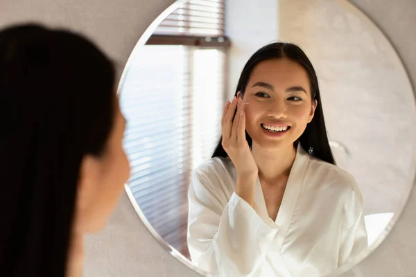 Young beautiful korean lady using moisturising face cream — Stok Foto