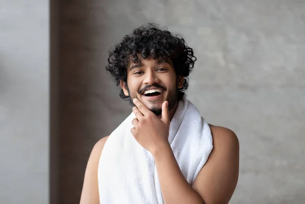 Portrait of happy bearded indian man with towel posing in bathroom and touching chin, ready to take bath — Φωτογραφία Αρχείου