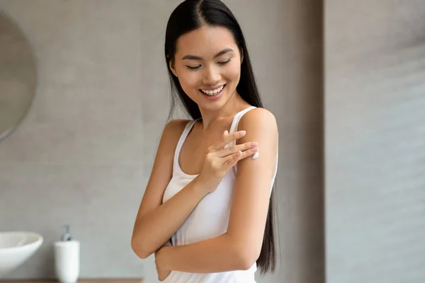 Happy asian woman applying skin butter on her shoulder — Φωτογραφία Αρχείου