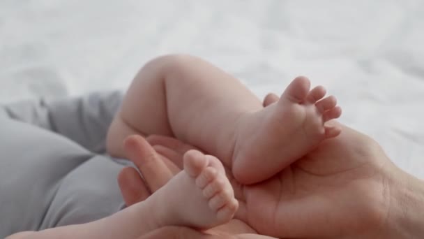 Любимая мама играет с крошечными ножками своего новорожденного ребенка дома — стоковое видео