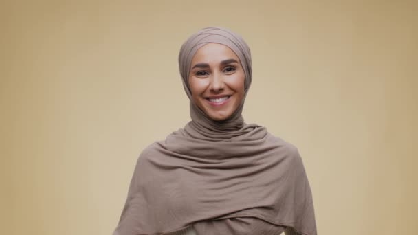 Concept de salutation. Jeune femme du Moyen-Orient parlant positif portant hijab agitant la main à la caméra et souriant — Video