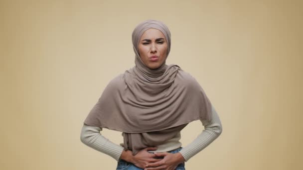 Buksmärta. Studio porträtt av unga mellanösternmuslimska dam bär hijab lider av magont — Stockvideo