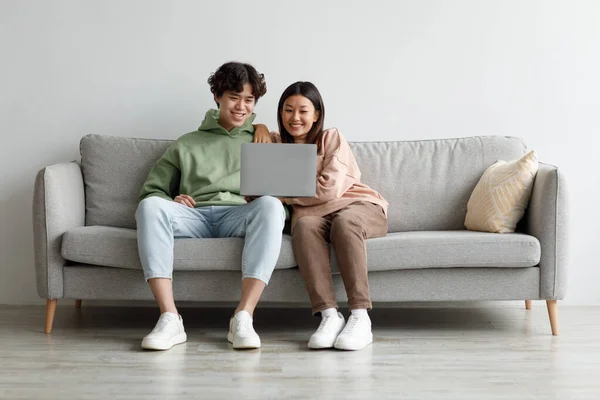 Любляча азіатська пара дивиться відео на ноутбуці, насолоджується вільним часом, сидить вдома на дивані, копіює простір. — стокове фото