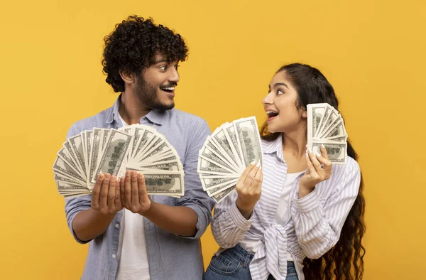 Pareja india emocional sosteniendo un montón de billetes de dinero y mirándose el uno al otro, fondo amarillo — Foto de Stock