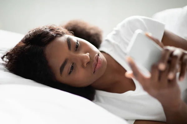 Afectado señora afroamericana usando teléfono inteligente en la cama —  Fotos de Stock