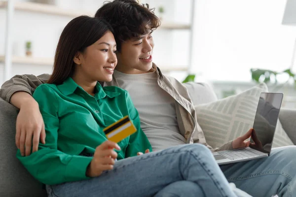 Jeune couple asiatique marié avec ordinateur portable et carte de crédit acheter des biens en ligne, en utilisant PC moderne pour les achats à distance à la maison — Photo