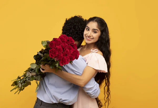 Feliz señora india abrazando a su novio y sosteniendo ramo de rosas, celebrando el Día de San Valentín sobre fondo amarillo — Foto de Stock