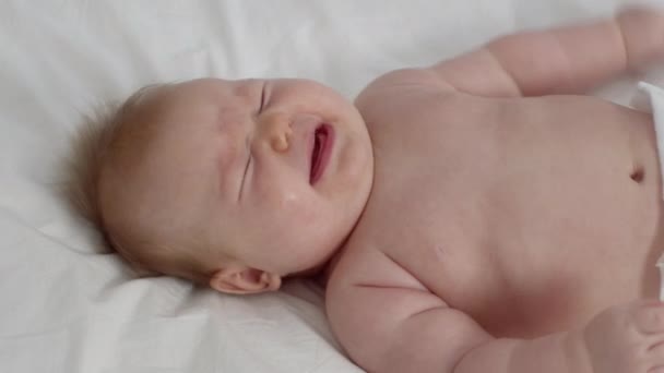 Sevimli küçük bebek yatakta uzanıp kameraya bakarken ağlıyor. — Stok video