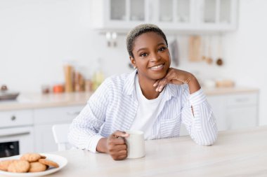 Mutlu bin yıllık güzel siyah kadın ve favori içeceği masada kurabiyelerle oturuyor.