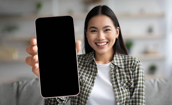 Femmina coreana sorridente che tiene grande smartphone con schermo vuoto a casa — Foto Stock