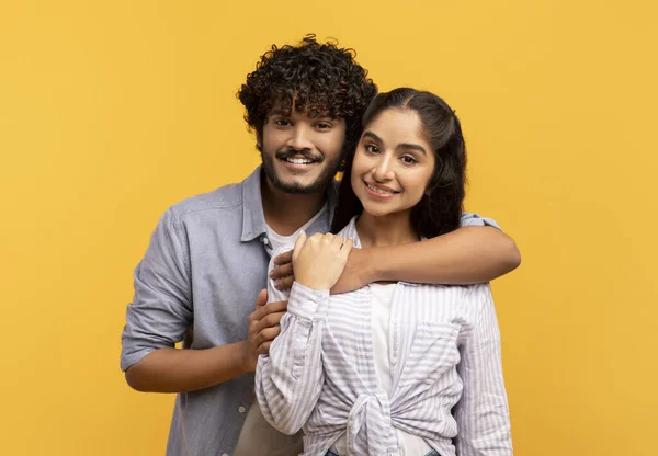 Couple amoureux. Amoureux indien homme étreignant sa petite amie de dos, debout ensemble sur fond jaune studio — Photo