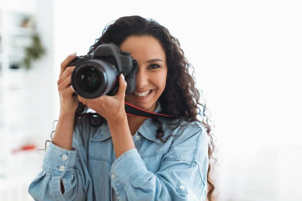 Feliz fotógrafo senhora tirando foto segurando câmera perto do rosto dentro de casa — Fotografia de Stock