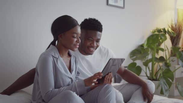 网络幽默。年轻快乐的非洲裔美国夫妇坠入爱河，在网上看社交媒体上有趣的视频，笑着 — 图库视频影像