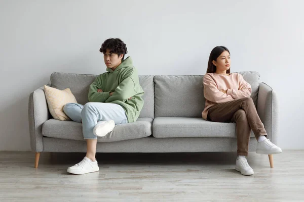 Irritado jovem casal asiático sentado no sofá em silêncio após a luta, olhando em direções opostas em casa — Fotografia de Stock