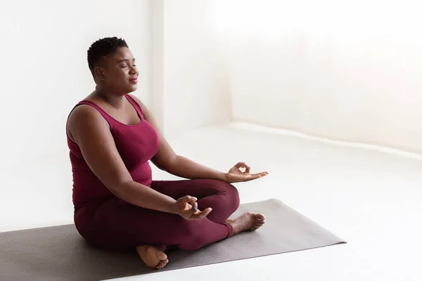 Pacífica señora negra gorda en ropa deportiva meditando en casa —  Fotos de Stock