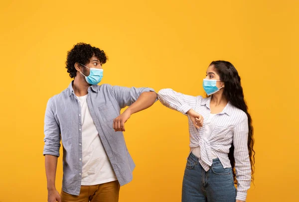 新颖的问候语,防止考拉病毒的传播.戴口罩的印度年轻夫妇碰碰肘部，黄底 — 图库照片