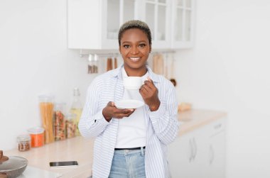Neşeli, güzel, bin yıllık siyah kadın, günlük giysiler içinde en sevdiği sıcak içeceği beyaz bardakta içiyor.