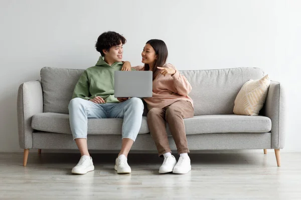 Millennial Asian couple using laptop computer together, sitting on sofa at home, free space — Stock Photo, Image