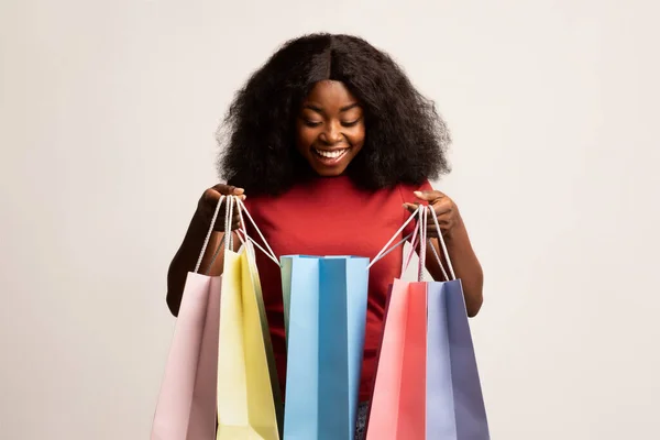 Сезонные продажи. Черная женщина держит сумки и заглядывает внутрь с волнением — стоковое фото
