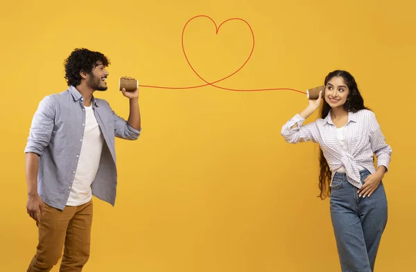 Pesan cinta. Loving indian man telling romantic words to girlfriend through tin can phone with heart shaped string — Stok Foto