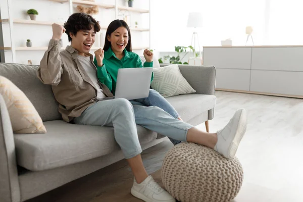 Couple asiatique émotionnel avec ordinateur portable faisant geste OUI, célébrant le succès, assis sur le canapé à la maison, espace libre — Photo