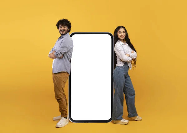 Pareja india milenaria apoyada en un smartphone gigante con maqueta, promocionando aplicación móvil o sitio web —  Fotos de Stock