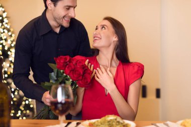 Genç yakışıklı adam kırmızı gülleri kadına veriyor.