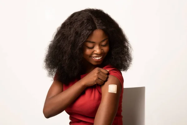 Koncepcja odporności. Zaszczepiona czarna kobieta patrząca na jej ramię z bandażem samoprzylepnym — Zdjęcie stockowe