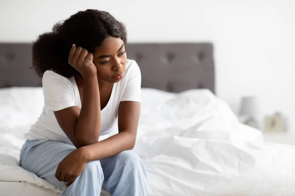 Deprimida afro-americana sentada na cama em casa — Fotografia de Stock