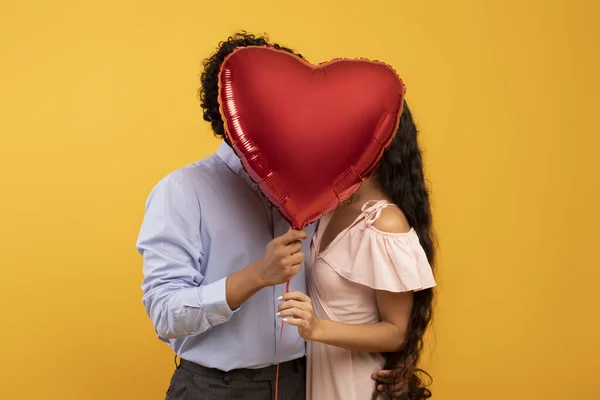 Romance, amor, aniversário ou dia dos namorados. Lovilng casal indiano beijando e fechando com balão de coração — Fotografia de Stock