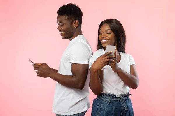 Casal afro-americano usando smartphones, parede de estúdio rosa — Fotografia de Stock