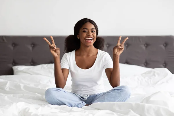 Позитивная африканская американка в пижаме сидит на кровати — стоковое фото