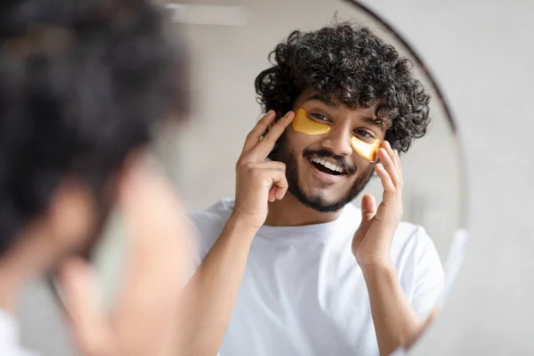 Porträtt av indian man applicera ögonlappar på ansiktet och titta på spegel på badrummet — Stockfoto