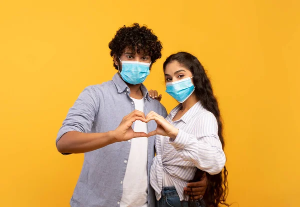 발렌틴 은 코로나 바이러스의 날이지. 보호 마스크를 쓰고 손으로 심장을 만들고 있는 로맨틱 한 인도의 배우자들 — 스톡 사진